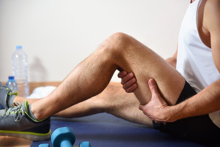 The image shows a person seated on the floor, stretching their leg while holding their thigh, likely engaging in post-exercise muscle recovery. This suggests an individual adopting an active lifestyle, focusing on fitness and well-being. A set of light weights is visible nearby, emphasizing the theme of regular physical activity.