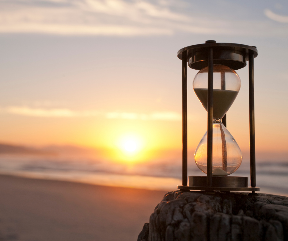 Hourglass on a beach log at sunset with the ocean in the background.