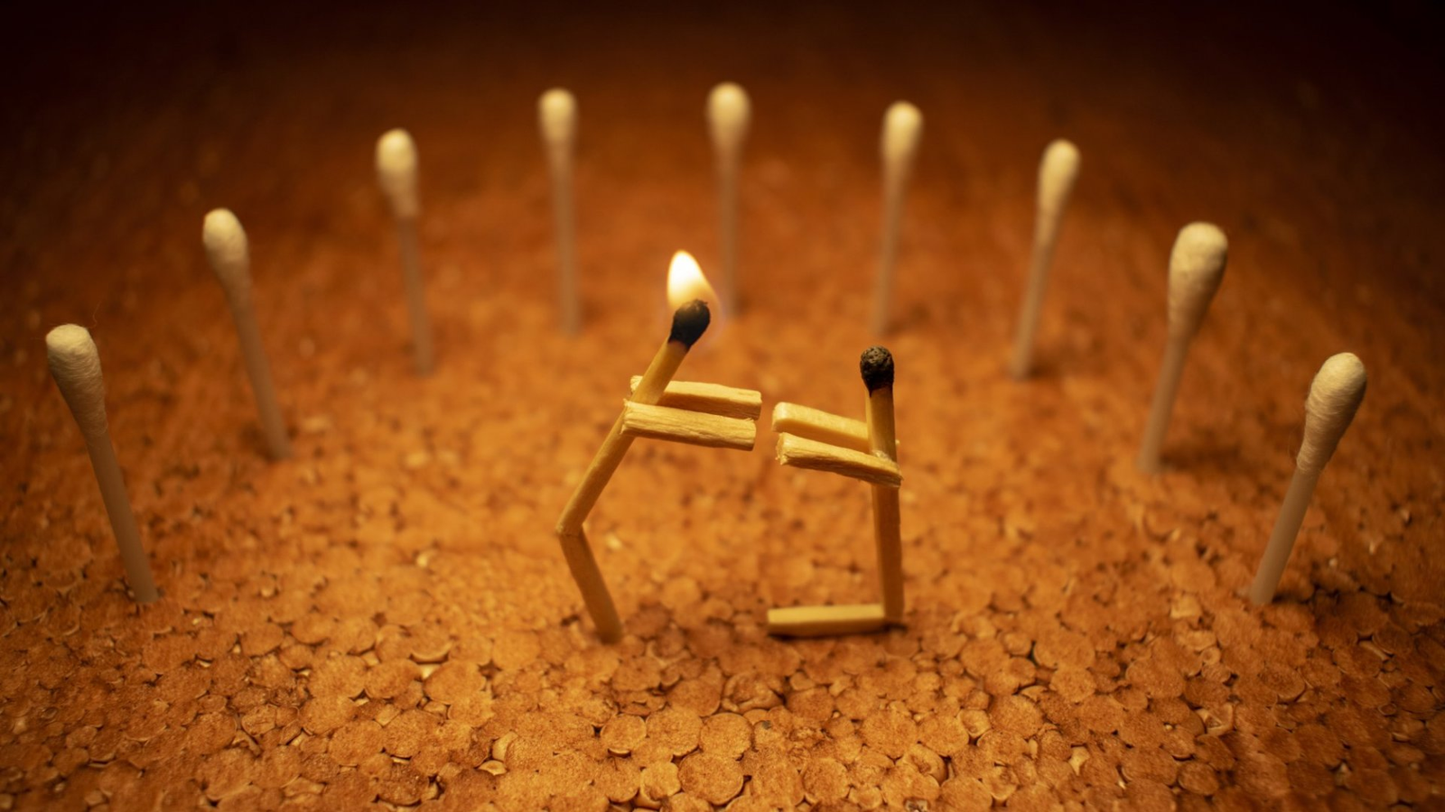 A lit matchstick figure surrounded by unlit matches on a textured surface.