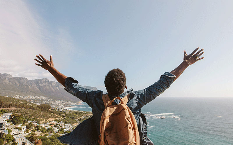 Person with arms outstretched facing a scenic coastal landscape.