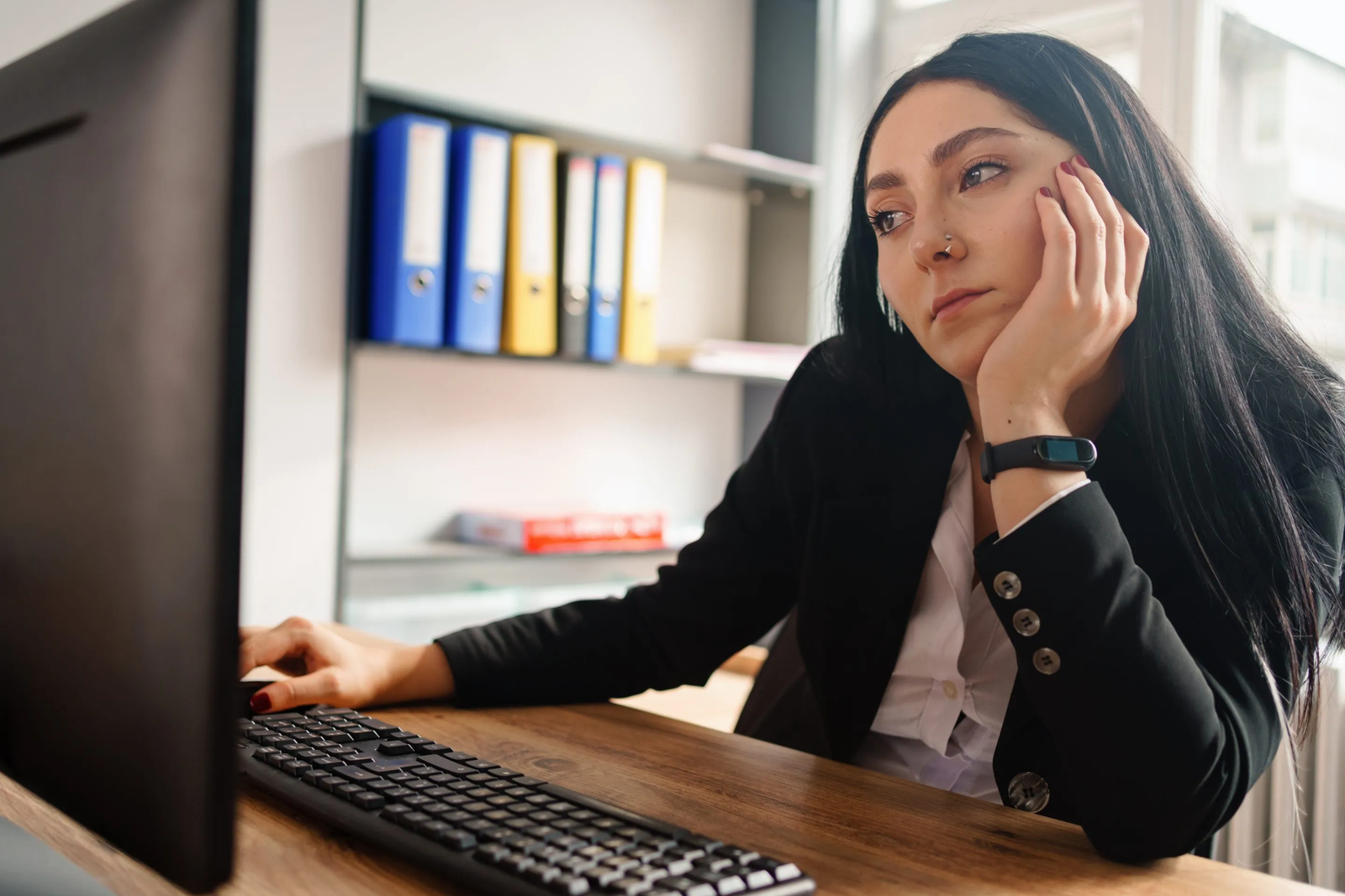 Woman at desk with computer, looking stressed or tired, hand on forehead.