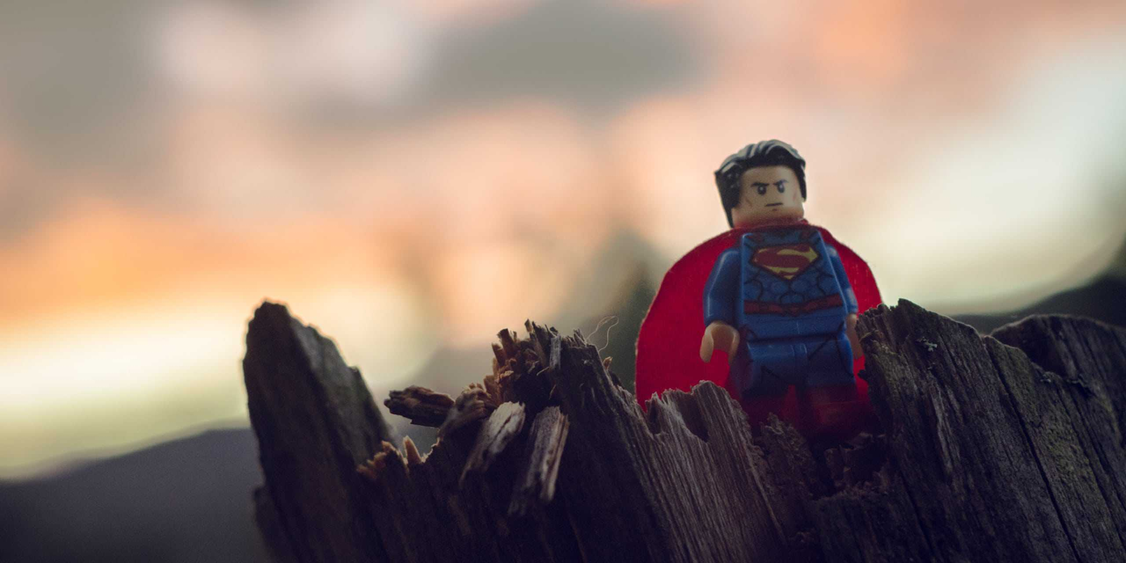 A Superman figurine stands atop a rugged stump against a twilight sky 