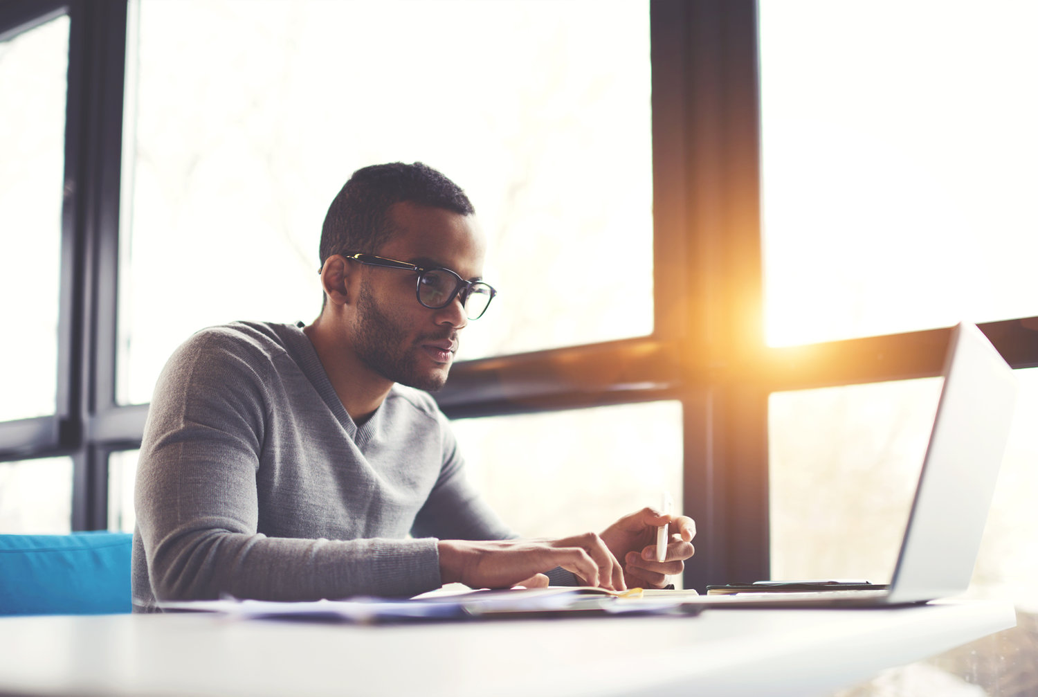 Person working on a laptop near a sunny window with a coffee cup.