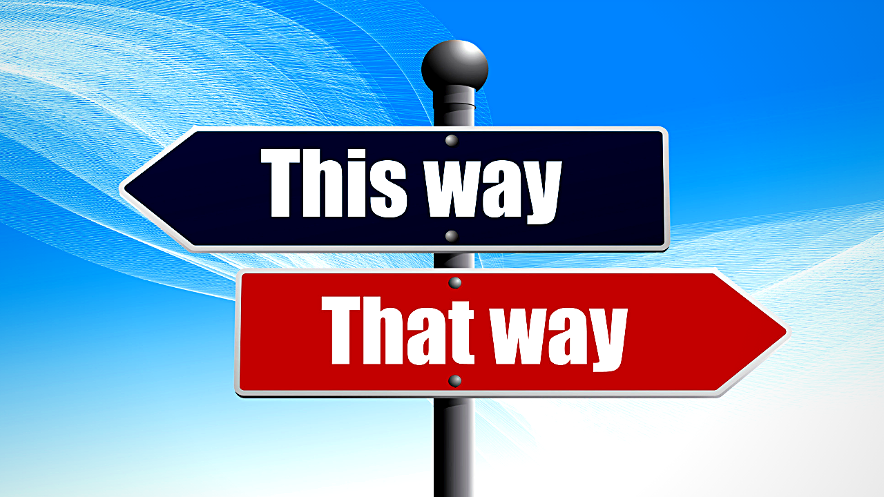  Two directional signs on a pole against a blue sky. The top sign reads "This way" in white on a dark background, and the bottom sign reads "That way" in white on a red background.