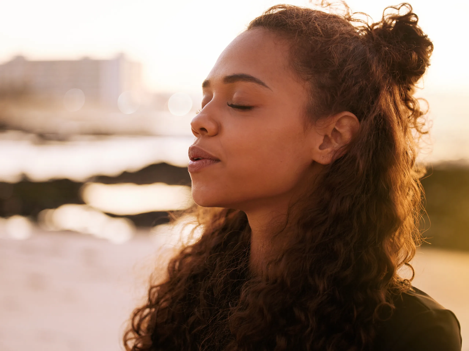 Person with curly hair looking away towards a sunlit beach.