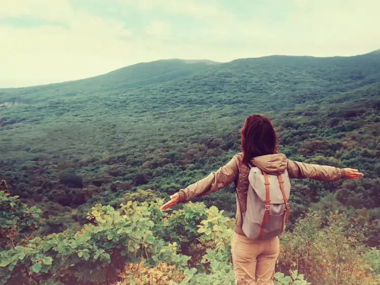 Person with open arms facing a lush green hillside.