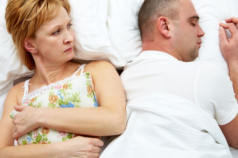 Two people lying in bed with their backs turned to each other.