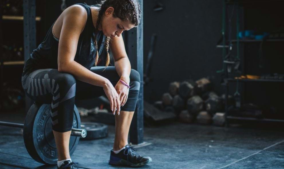 Person in workout gear resting on a weightlifting plate in a gym.