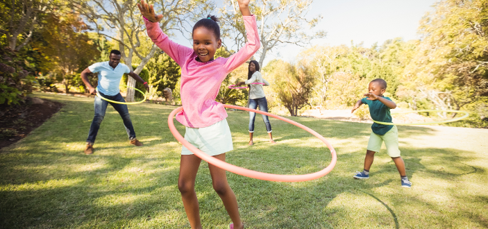 Family enjoying hula hooping together on a sunny day outdoors.