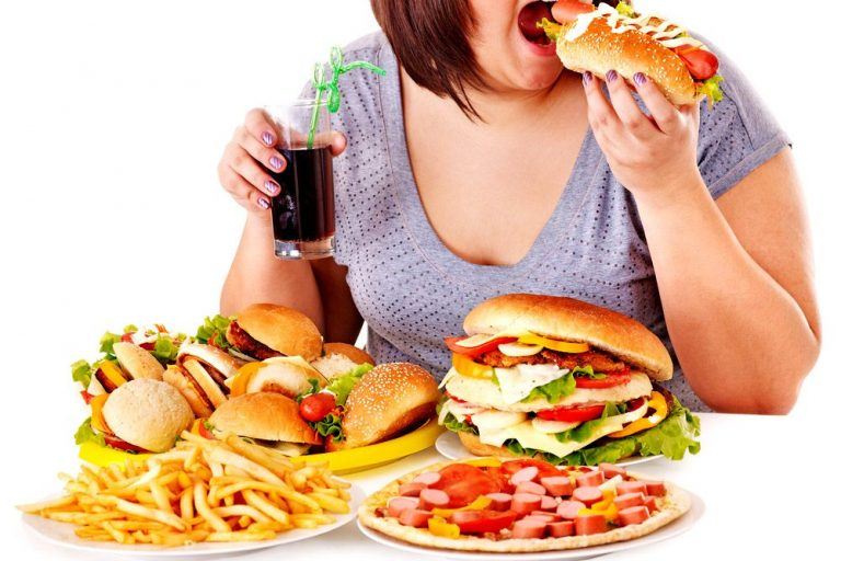 Person eating a burger with a table full of fast food and soda.