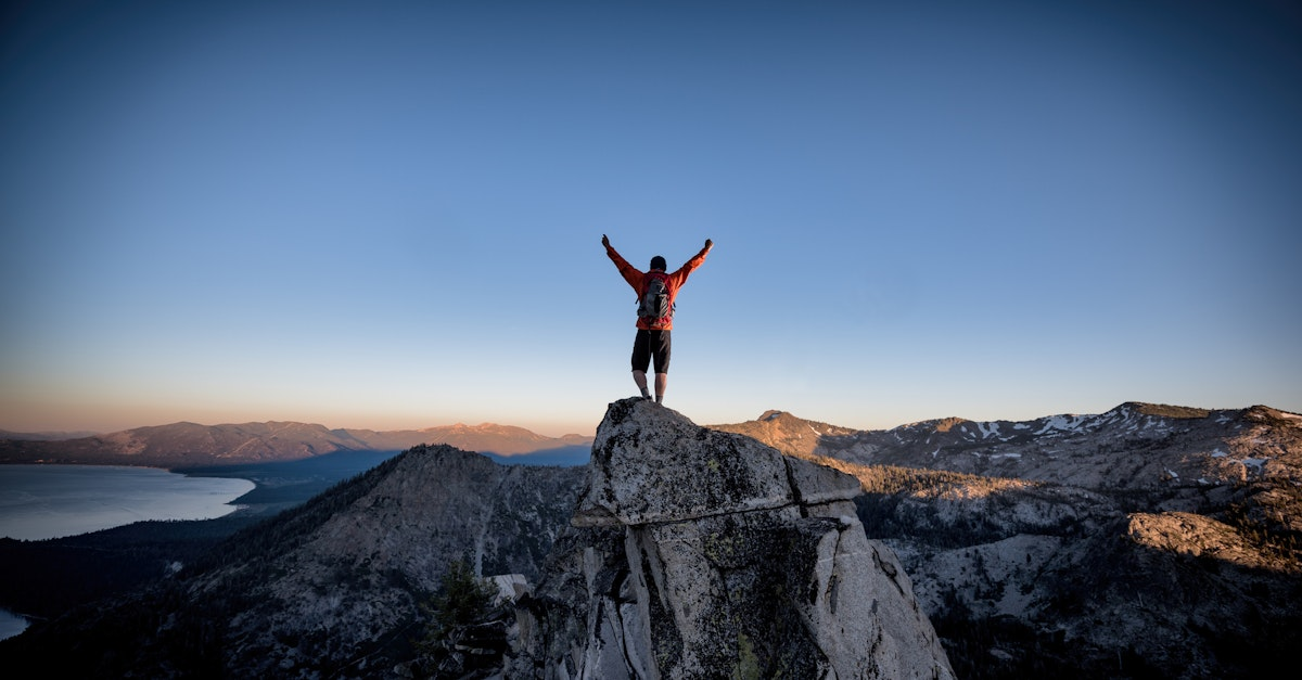 Person on a mountaintop with arms raised against a dusk sky.